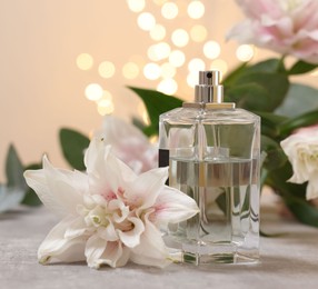 Bottle of perfume and beautiful lily flowers on table against beige background with blurred lights, closeup