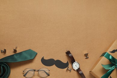 Gift box, paper mustache and men accessories on brown background, flat lay with space for text. Father's day celebration