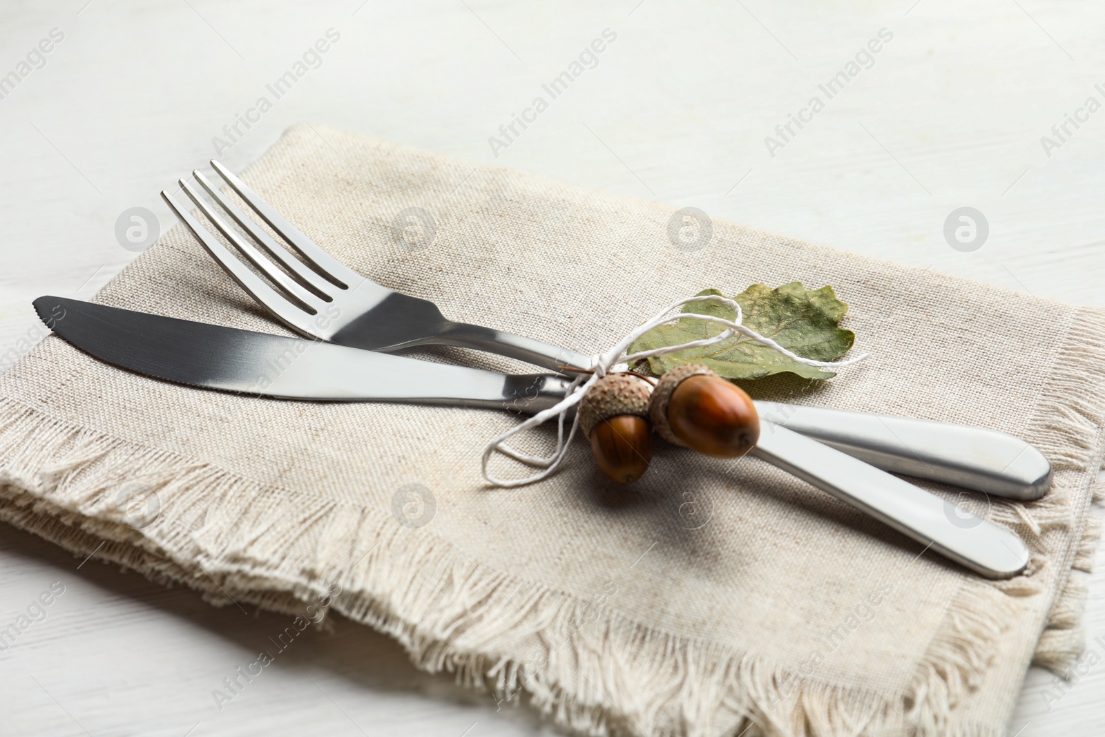 Photo of Cutlery with napkin, acorns and napkin on white wooden background, closeup. Table setting elements