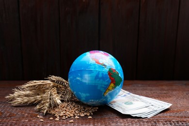 Photo of Globe, ears of wheat and banknotes on wooden table. Import and export concept