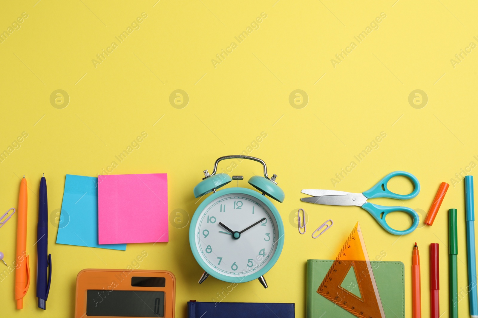 Photo of Flat lay composition with alarm clock and different stationery on yellow background, space for text. School time