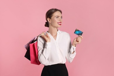 Happy young woman with shopping bags and credit card on light pink background. Big sale