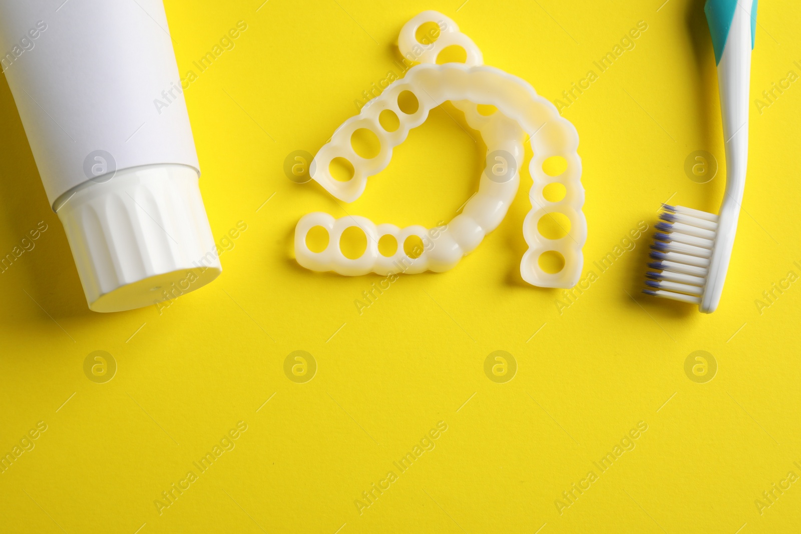 Photo of Bite correction. Toothpaste, brush and dental mouth guards on yellow background, flat lay. Space for text