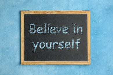 Small chalkboard with motivational quote Believe in yourself on light blue background, top view