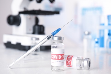 Vials with vaccine against Covid-19 and syringe on white table indoors