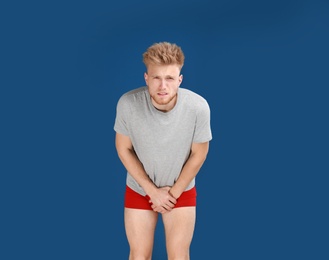 Photo of Young man suffering from pain on blue background. Urology problems