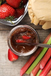 Tasty rhubarb jam, stems and strawberries on wooden table, flat lay