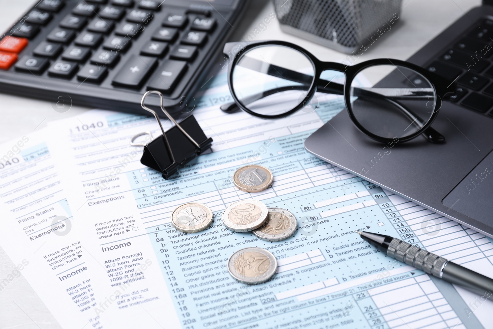 Photo of Tax forms, coins, stationery and calculator on table, closeup