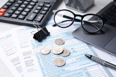 Photo of Tax forms, coins, stationery and calculator on table, closeup