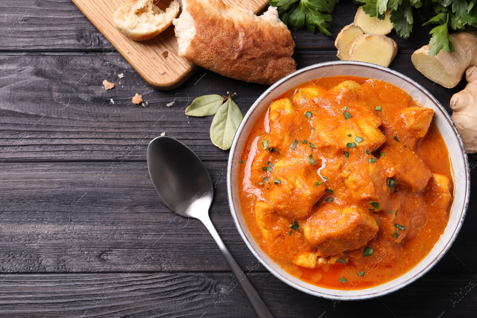 Photo of Bowl of delicious chicken curry on black wooden table, flat lay. Space for text