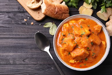 Bowl of delicious chicken curry on black wooden table, flat lay. Space for text