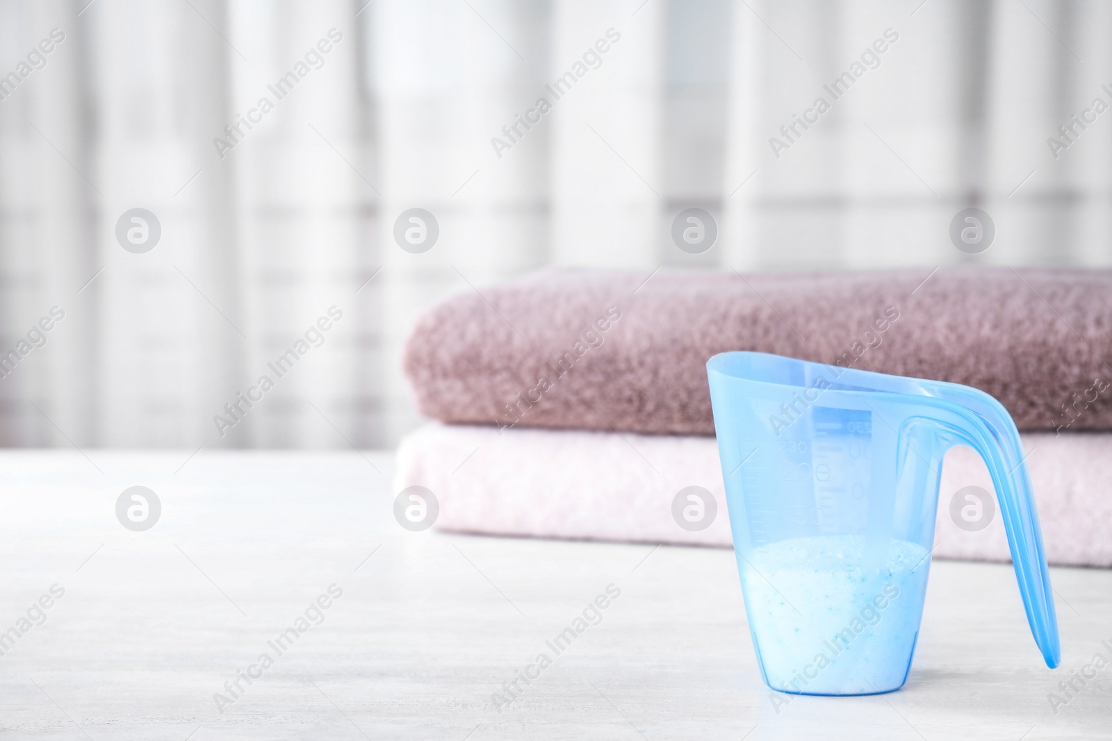 Photo of Measuring cup of washing powder on table against blurred background. Space for text