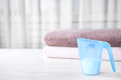 Photo of Measuring cup of washing powder on table against blurred background. Space for text