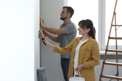 Woman and man hanging wallpaper in room