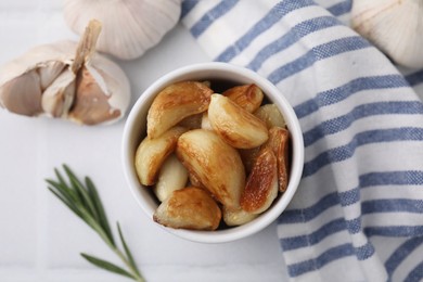 Photo of Fried garlic cloves in bowl and rosemary on table, flat lay