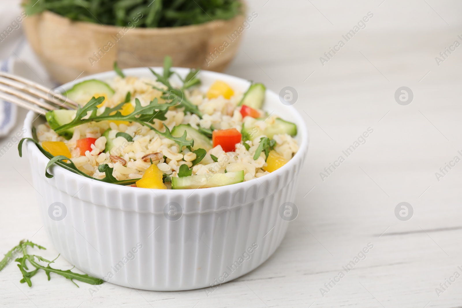 Photo of Cooked bulgur with vegetables in bowl on white wooden table, closeup. Space for text