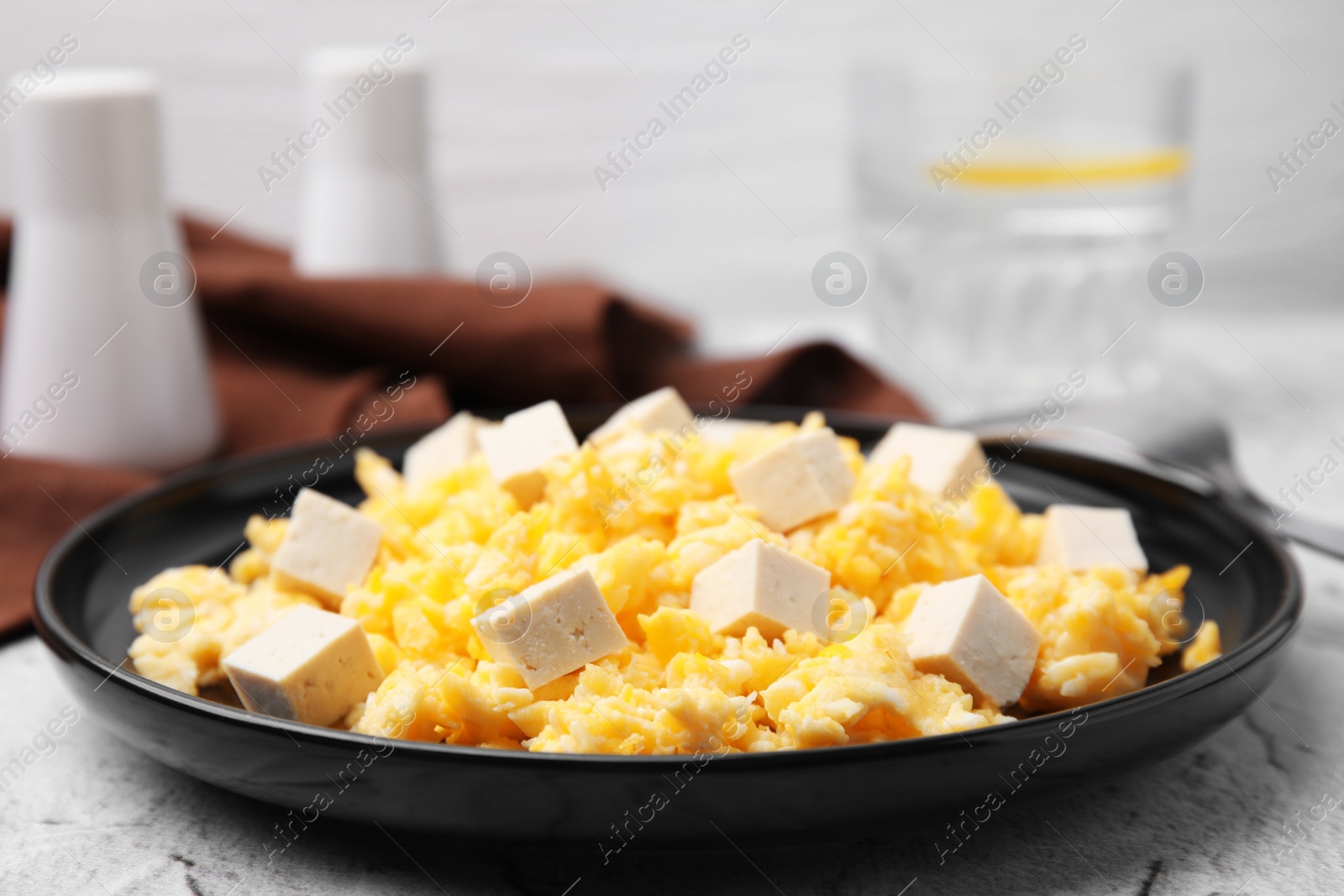 Photo of Plate with delicious scrambled eggs and tofu on white textured table