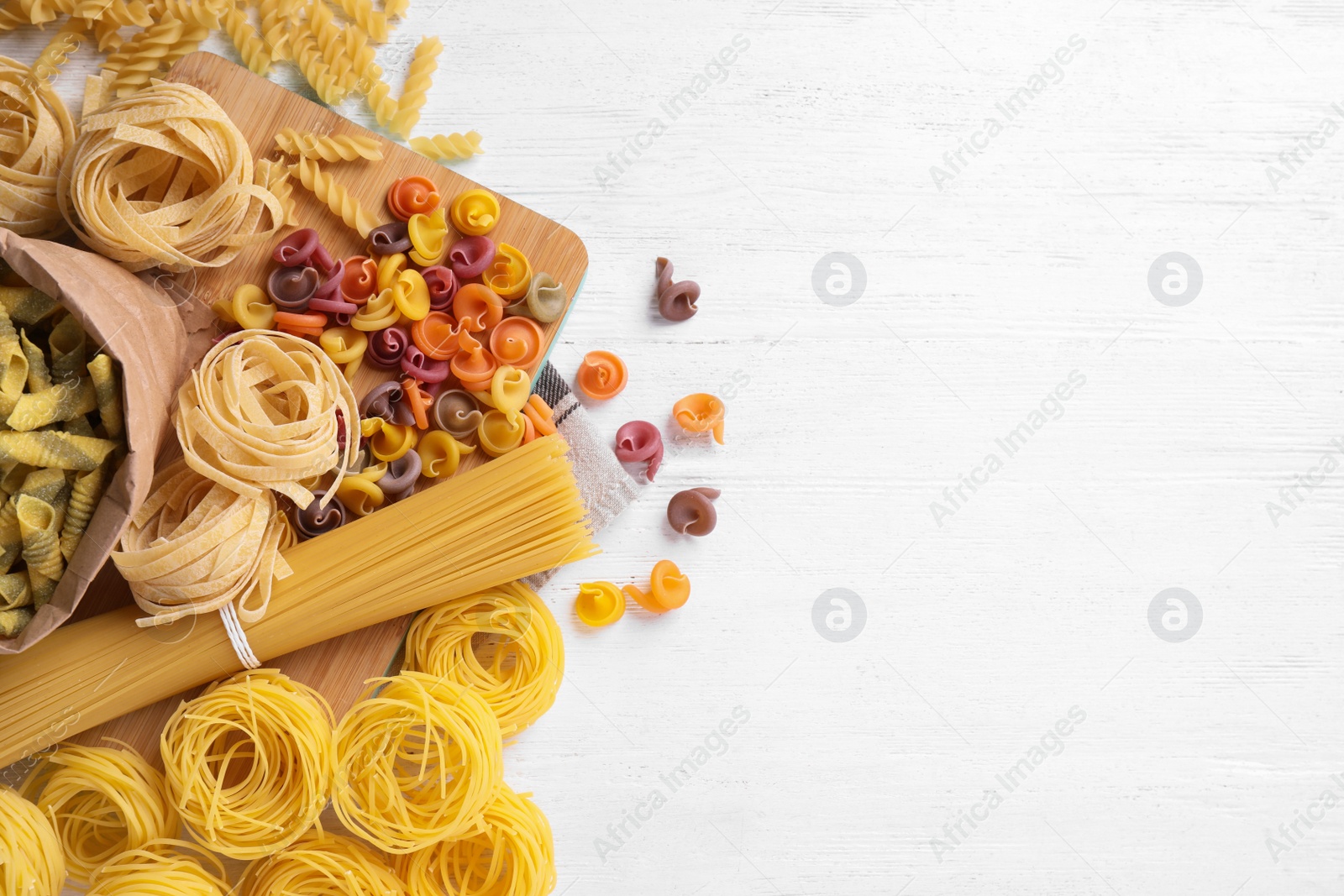 Photo of Different types of pasta on white wooden table, flat lay. Space for text