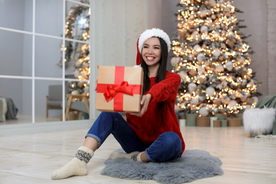 Photo of Happy young woman in Santa hat with Christmas gift at home