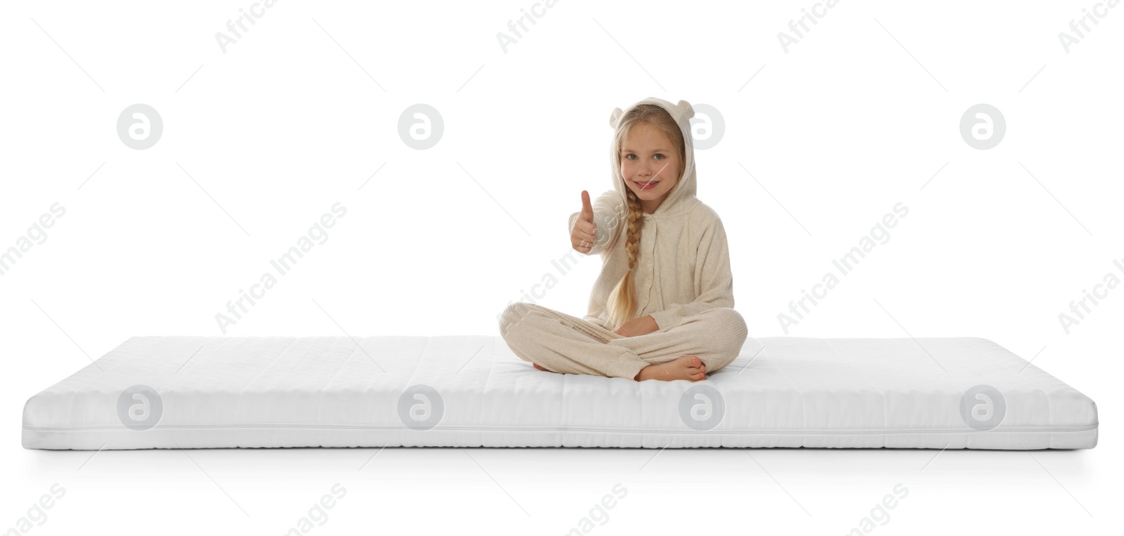 Photo of Little girl sitting on mattress and showing thumb up against white background