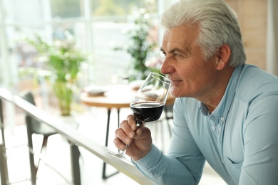 Photo of Senior man with glass of wine in restaurant. Space for text