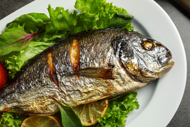 Photo of Delicious roasted fish with lemon and lettuce on plate, closeup view