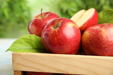 Photo of Wooden crate with ripe juicy red apples against blurred background, closeup