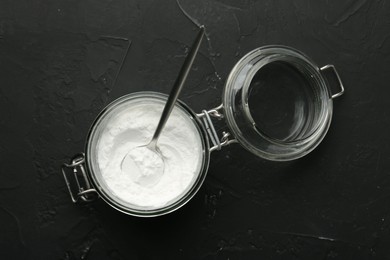 Photo of Baking powder in jar and spoon on black textured table, top view