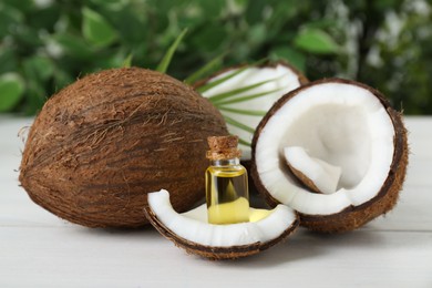 Photo of Bottle of organic coconut cooking oil, leaf and fresh fruits on white wooden table, closeup