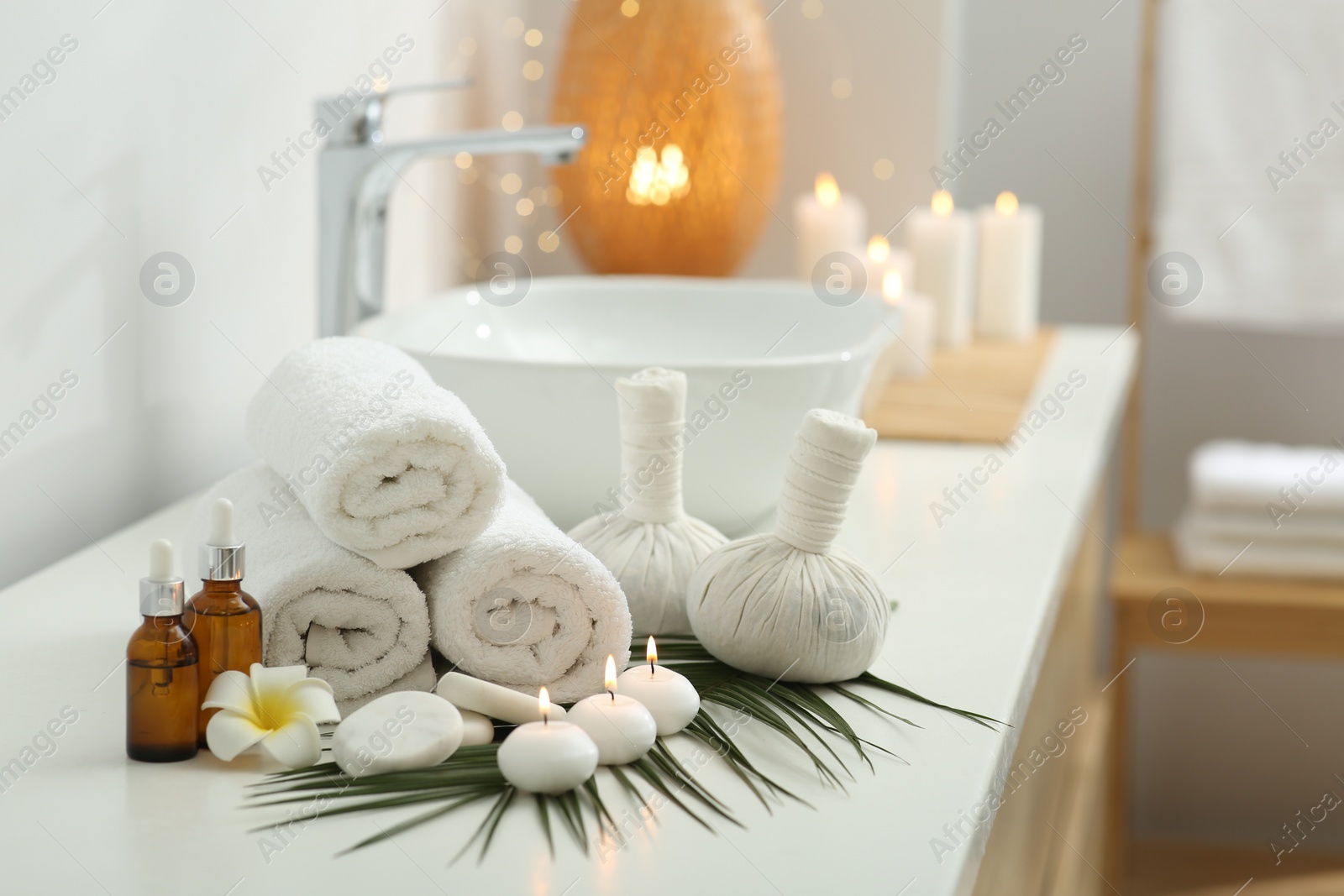 Photo of Spa composition. Rolled towels, herbal bags, cosmetic products and burning candles on white countertop in bathroom