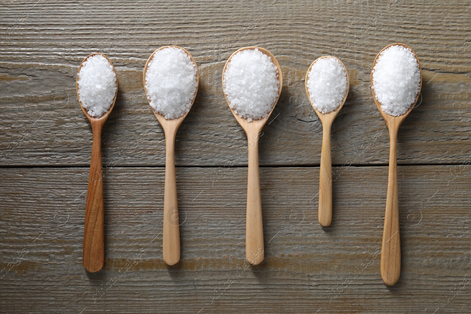 Photo of Organic salt in spoons on wooden table, flat lay