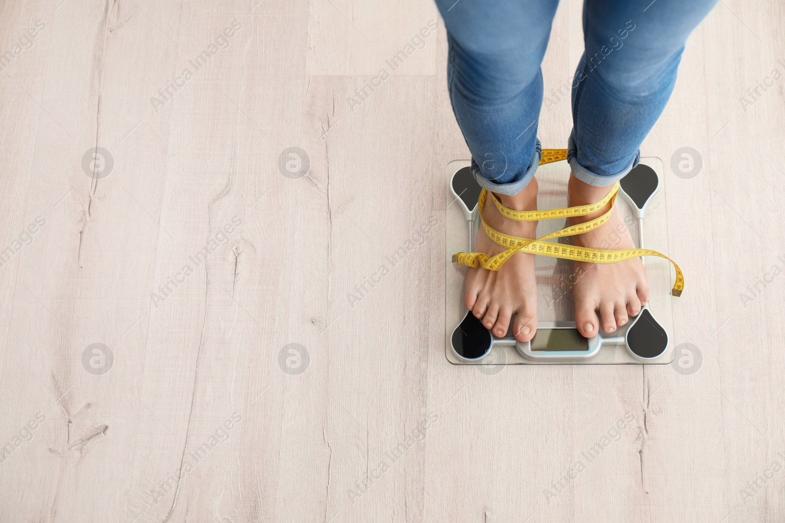 Photo of Woman with tape measuring her weight using scales on wooden floor, top view. Healthy diet