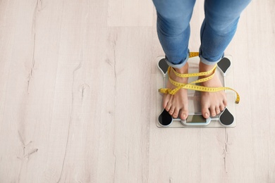 Photo of Woman with tape measuring her weight using scales on wooden floor, top view. Healthy diet