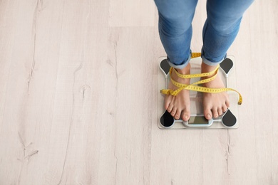 Woman with tape measuring her weight using scales on wooden floor, top view. Healthy diet