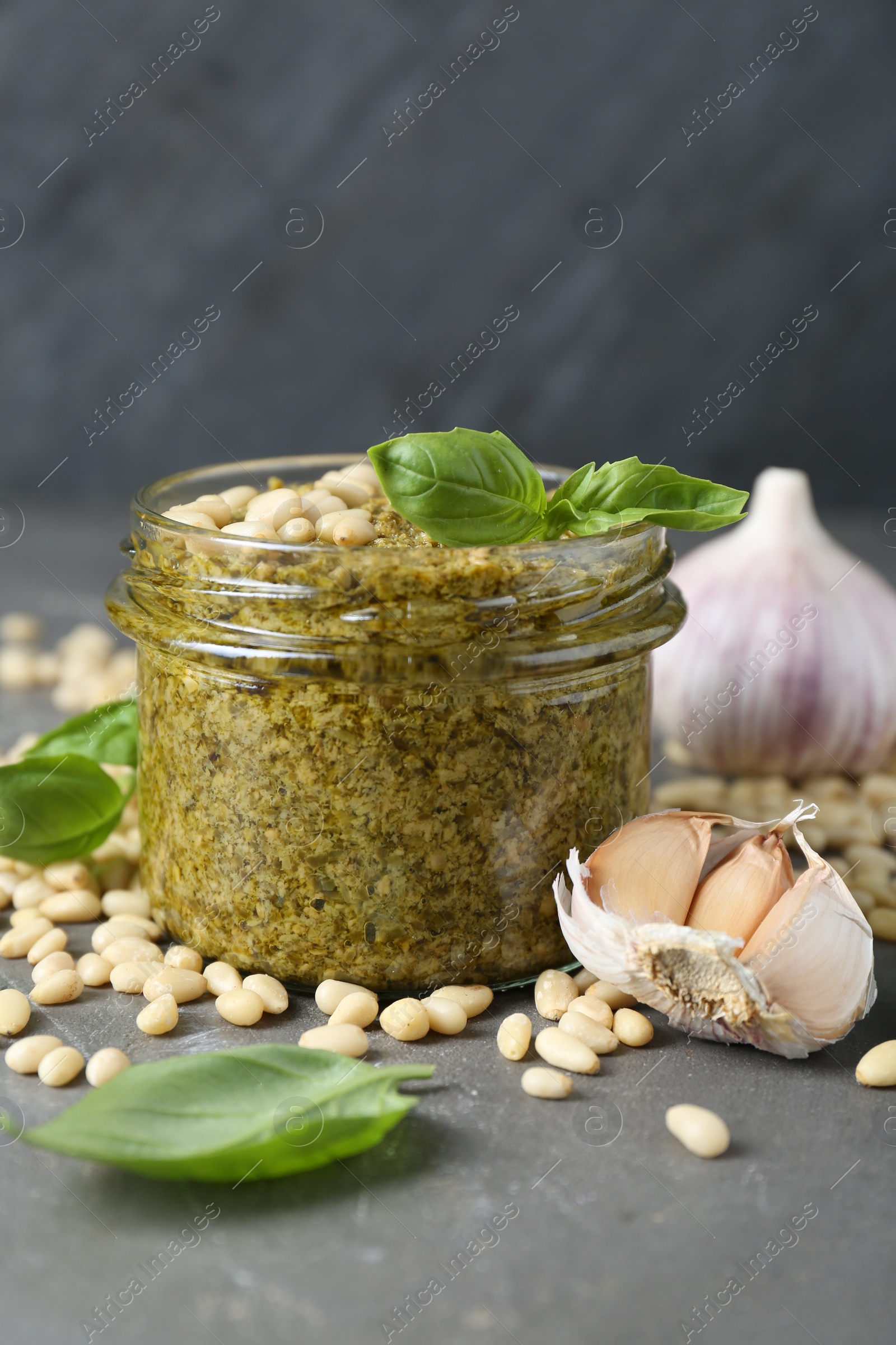 Photo of Jar of delicious pesto sauce and ingredients on grey table, closeup