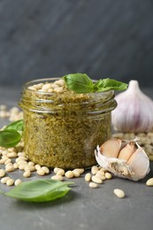 Jar of delicious pesto sauce and ingredients on grey table, closeup