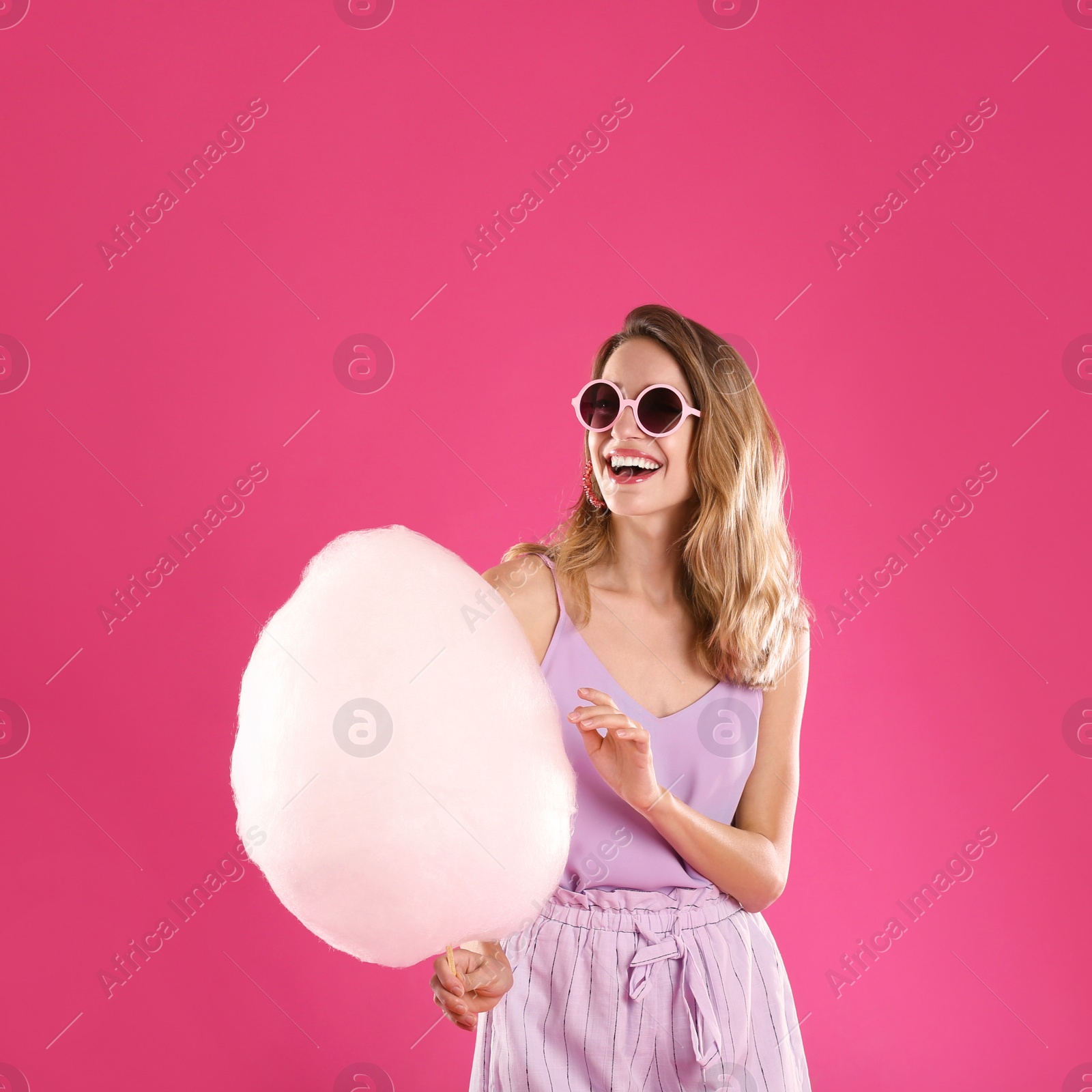 Photo of Happy young woman with cotton candy on pink background