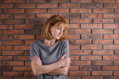 Photo of Senior woman suffering from depression near brick wall