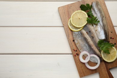 Photo of Delicious salted herring fillets served with lemon, parsley and onion rings on white wooden table, top view. Space for text