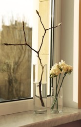Photo of Beautiful freesia flowers and tree branch with buds on window sill indoors. Spring time