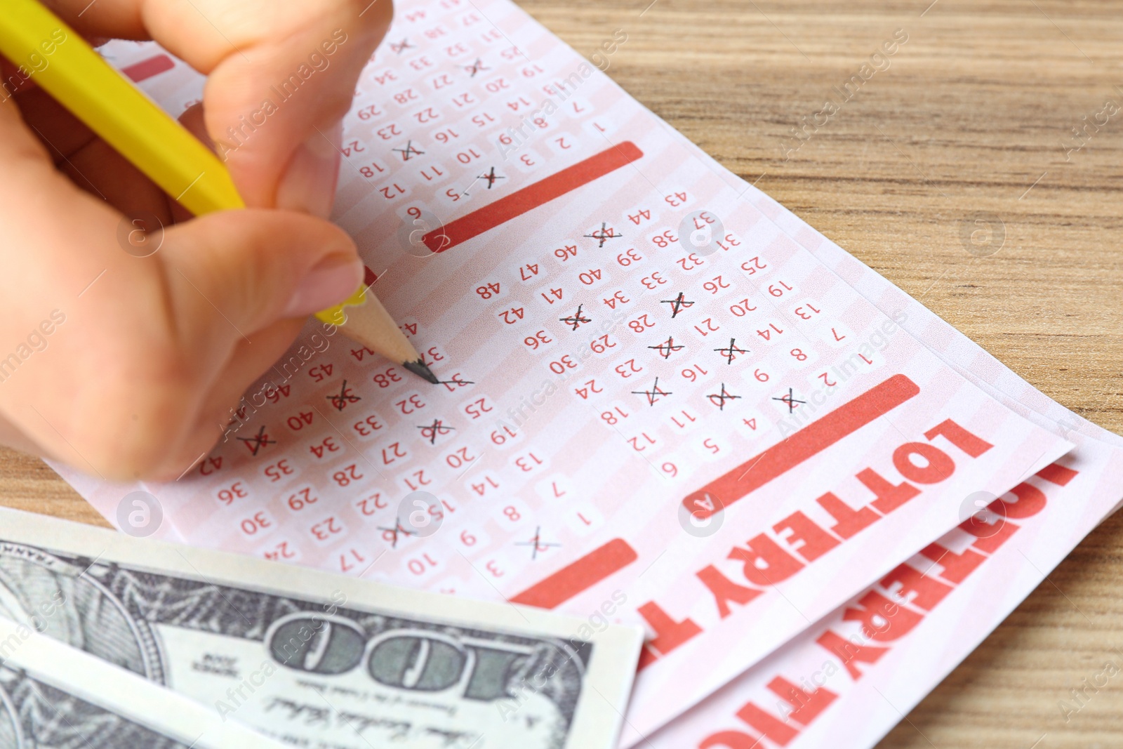 Photo of Woman filling out lottery tickets with pencil and money on wooden table, closeup. Space for text