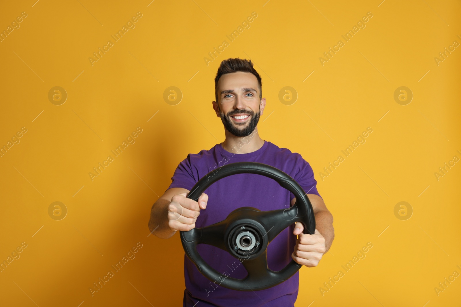Photo of Happy man with steering wheel on yellow background