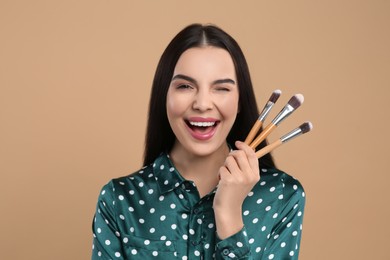 Happy woman with different makeup brushes on light brown background