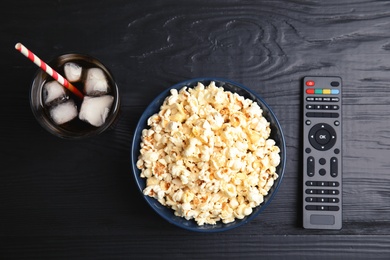 Bowl with popcorn, glass of iced cola and TV remote on wooden background, top view. Watching cinema