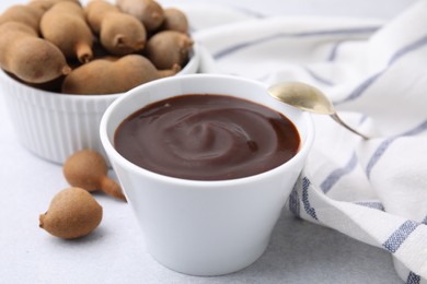 Photo of Bowl of tamarind sauce, spoon and fresh pods on light table, closeup