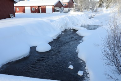 Picturesque view of frozen pond and houses on snowy day. Winter landscape