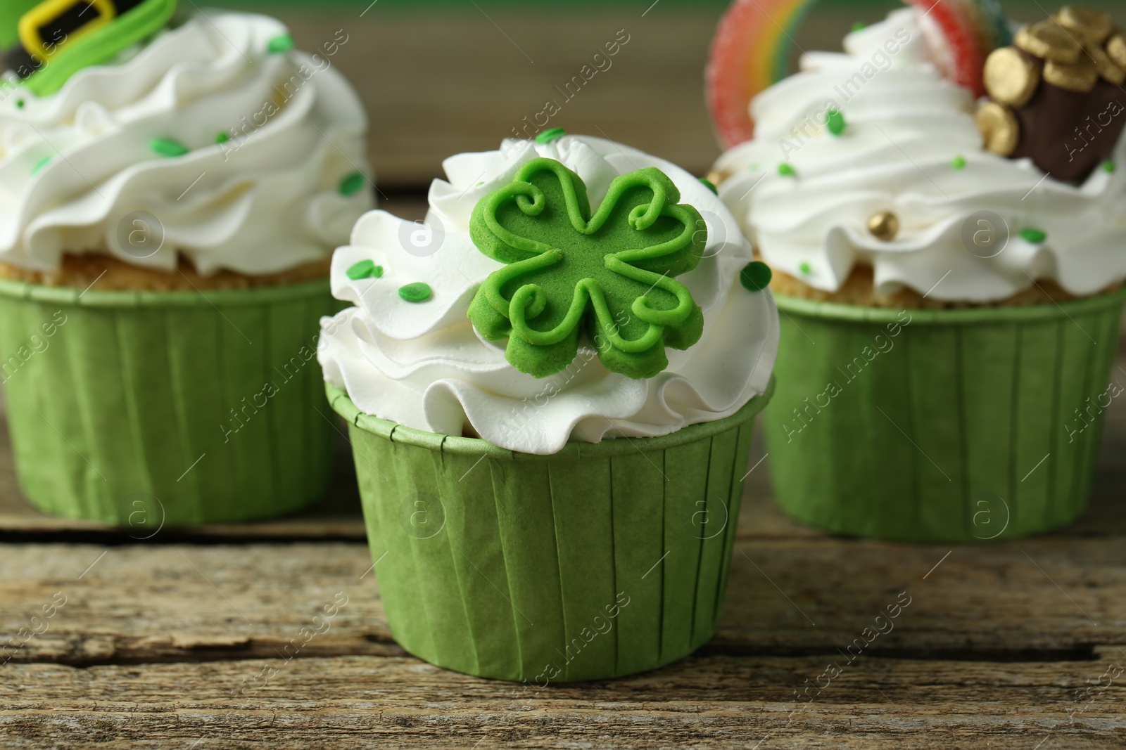 Photo of St. Patrick's day party. Tasty festively decorated cupcakes on wooden table, closeup