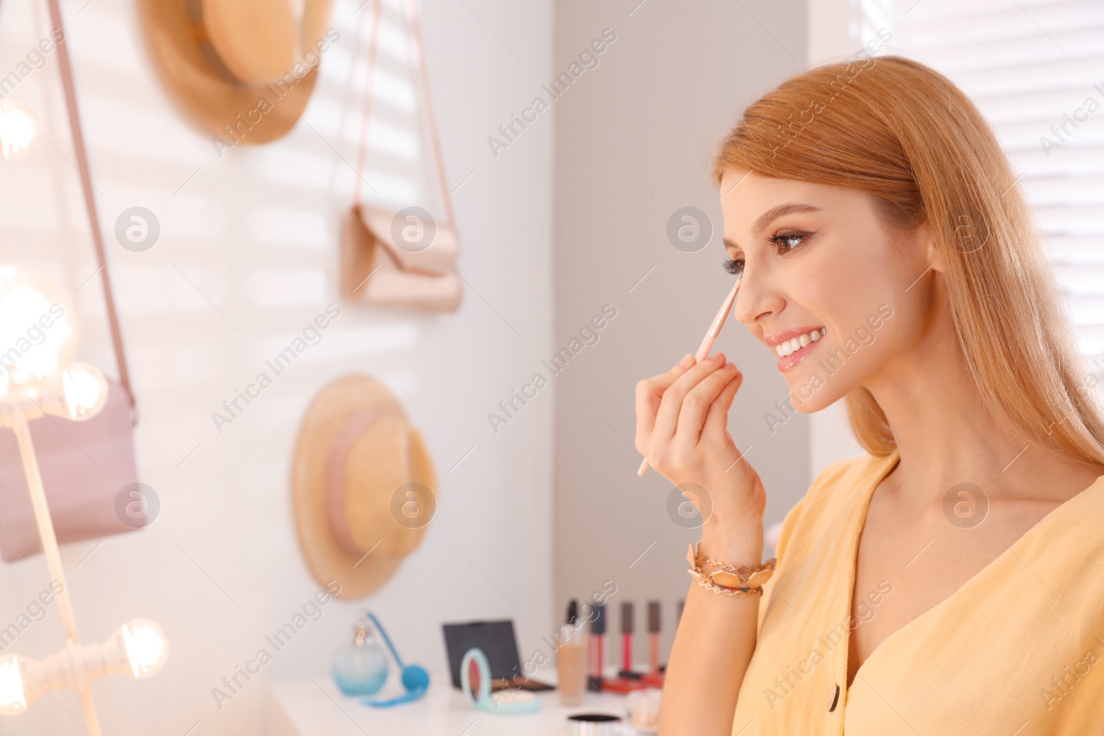 Photo of Beautiful young woman applying makeup near mirror in dressing room