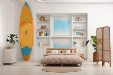 Photo of SUP board, bed and furniture in room. Interior design