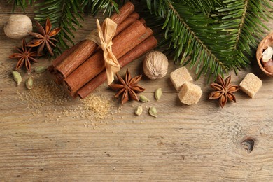 Photo of Different aromatic spices and fir branches on wooden table, flat lay. Space for text